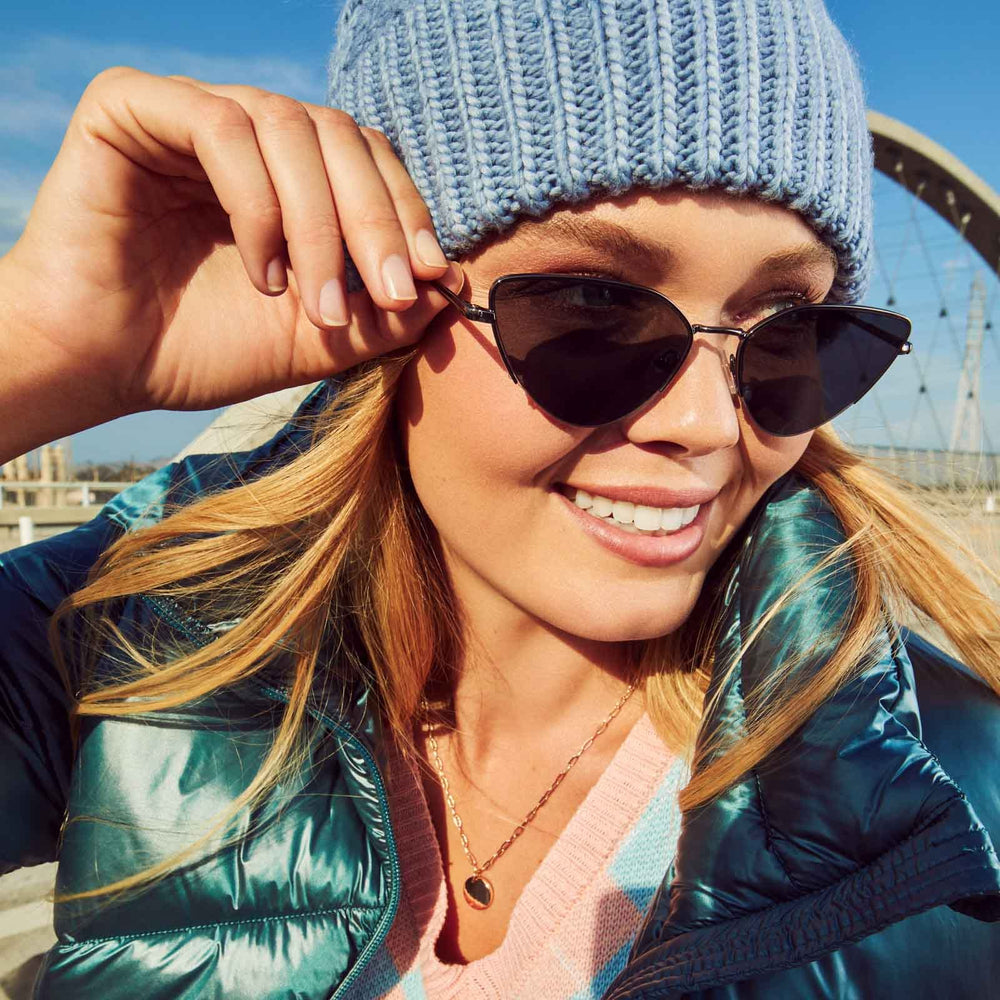 on model - female looking way from the sun while wearing dime optics fairfax cat eye sunglasses with a shiny gunmetal frame and solid grey lenses