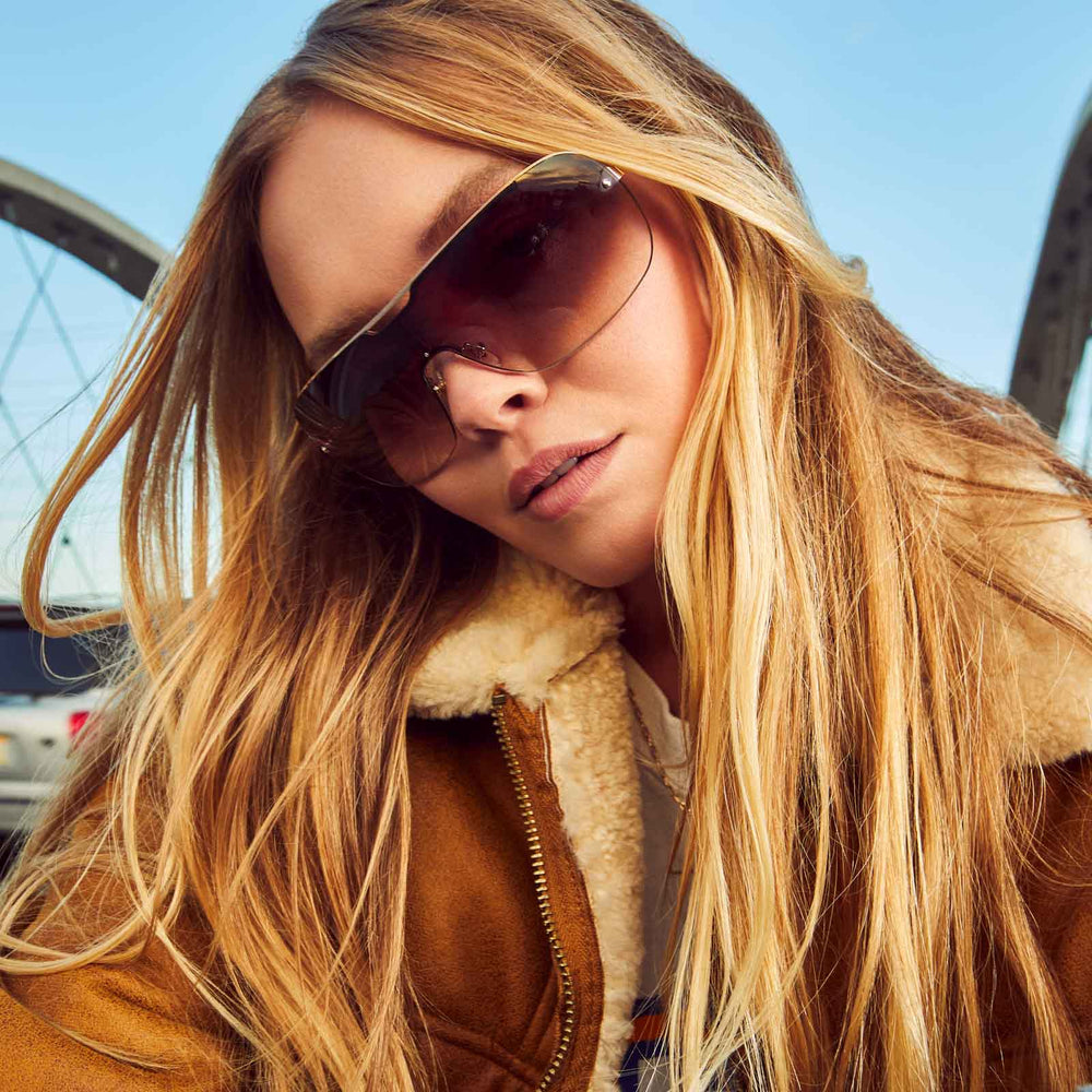 on model - female wearing dime optics wilshire shield metal sunglasses with a shiny gold frame and brown gradient sharp lenses