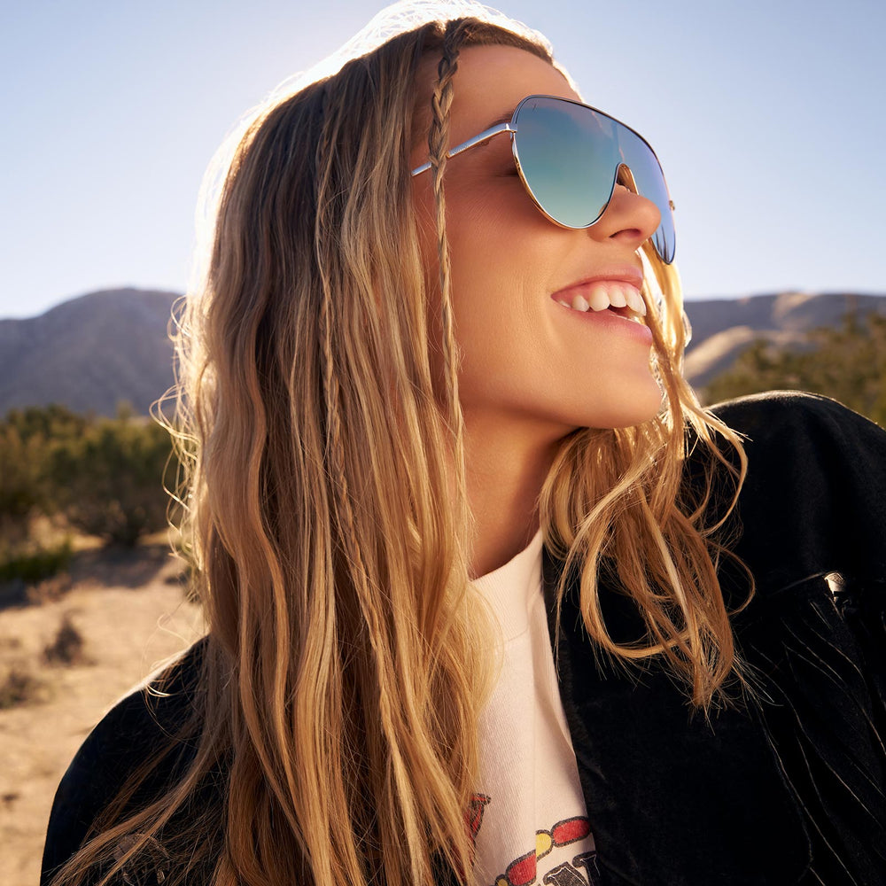 on model - female wearing dime optics tarzana shield sunglasses with a brushed gold metal frame and brown gradient polarized lenses side view