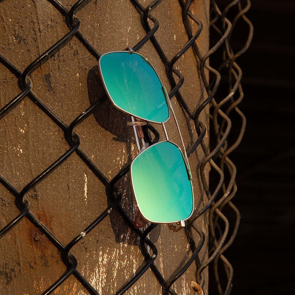 dime optics encino gold cyan mirror sunglasses hanging on a fence