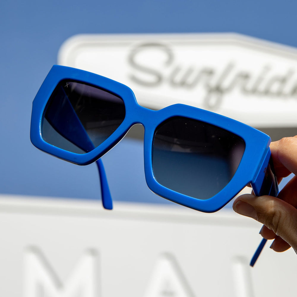 dime optics highland pool house blue with grey lenses sunglasses in front of a surf side sign