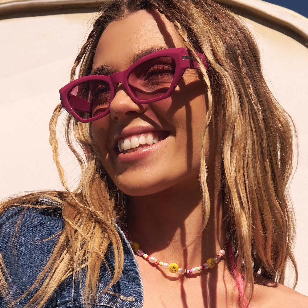 lifestyle - female wearing dime optics sawtelle cat eye sunglasses with a glossy berry frame and garnet gradient lenses angled view