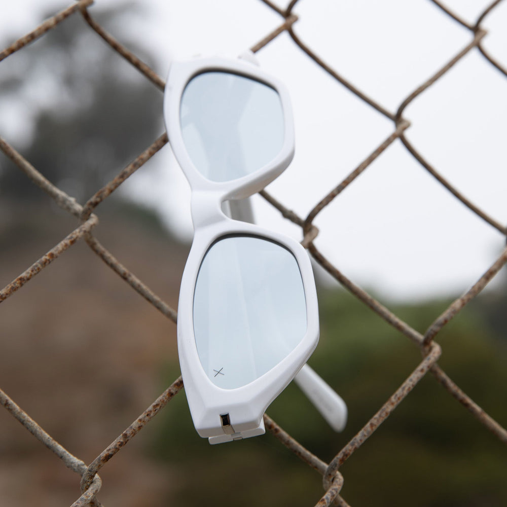 dime optics sawtelle cat eye sunglasses with a glossy white frame and silver mirror polarized lenses hanging on a fence