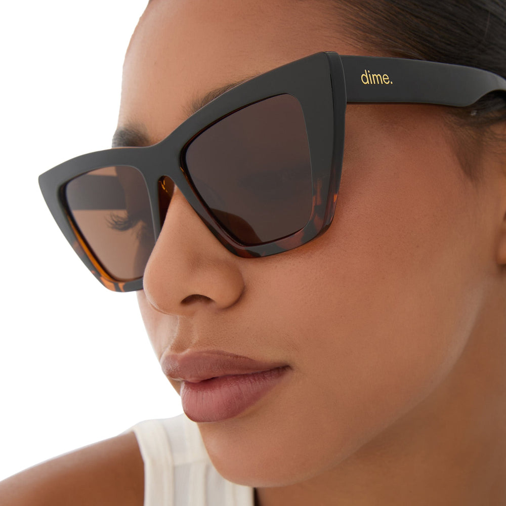 on model - female wearing dime optics featuring the windsor cat eye sunglasses with a black tortoise frame and brown polarized lenses angled view