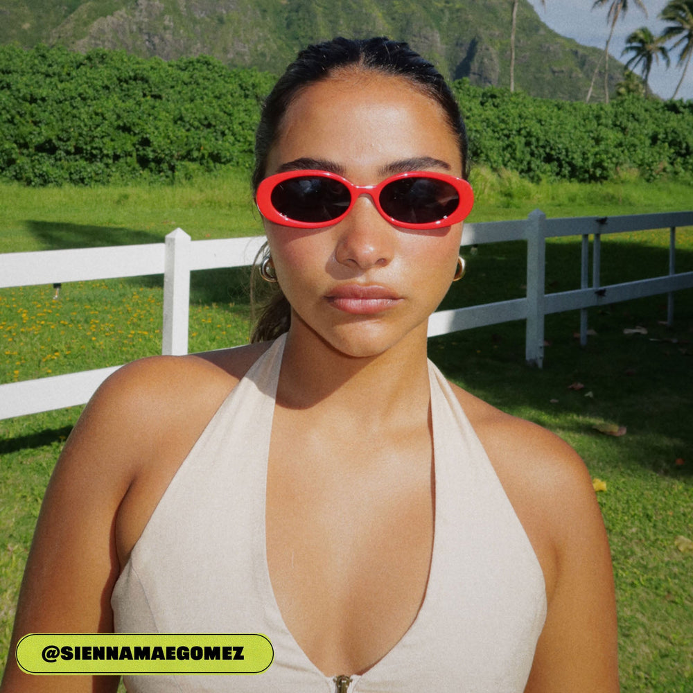 on model - sienna gomez female wearing dime optics westwood round sunglasses with a ruby red frame and grey polarized lenses front view