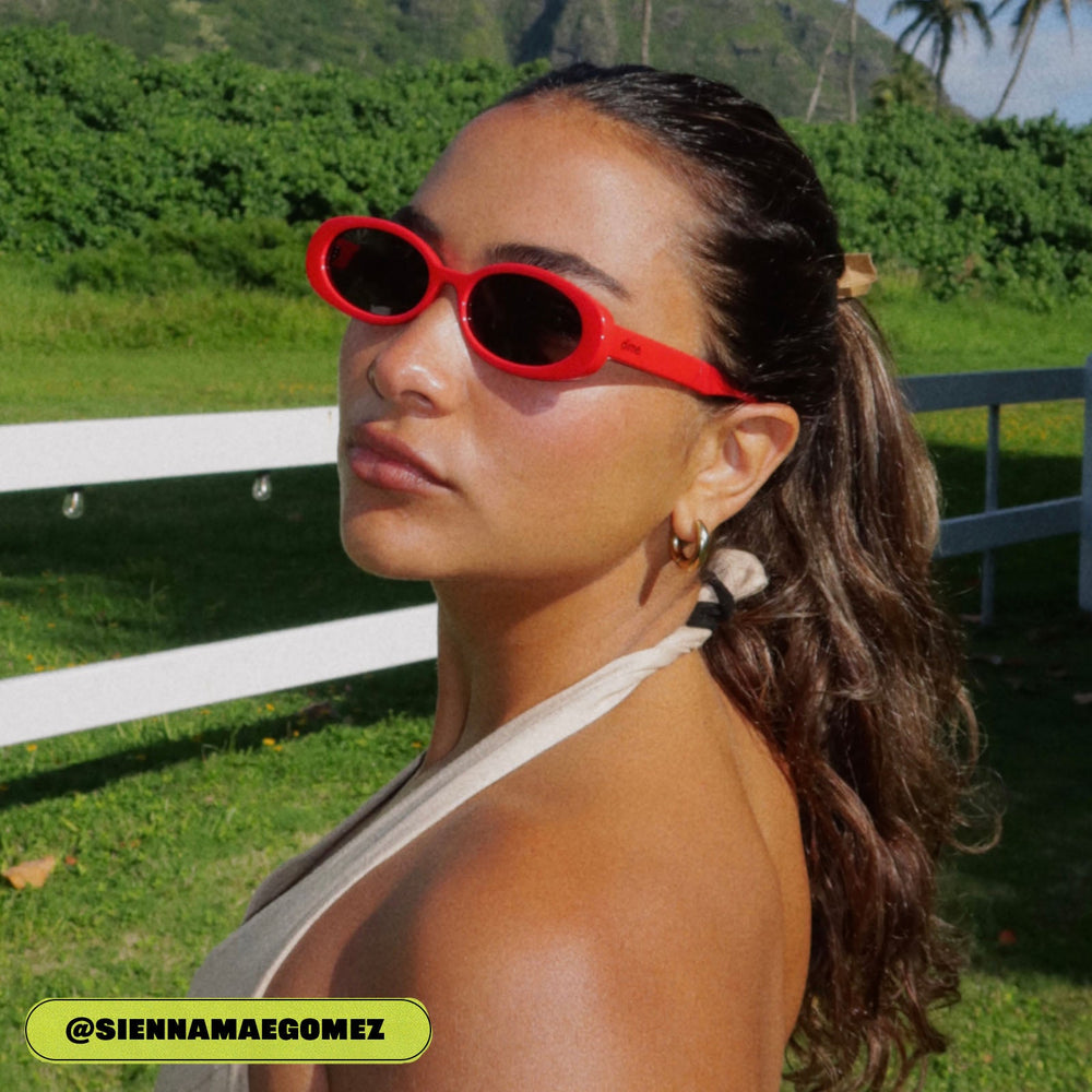 on model - sienna gomez female wearing dime optics westwood round sunglasses with a ruby red frame and grey polarized lenses angled view